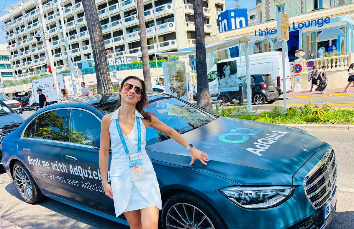 An AdQuick-wrapped Mercedes parked on a Cannes street reading Book me with AdQuick, with a team member standing beside it.