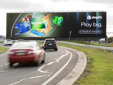 Billboard advertising on a major highway featuring a Toys"R"Us and Shopify co-branded out-of-home (OOH) campaign with the tagline "Play big" — large-format roadside billboard with high traffic visibility